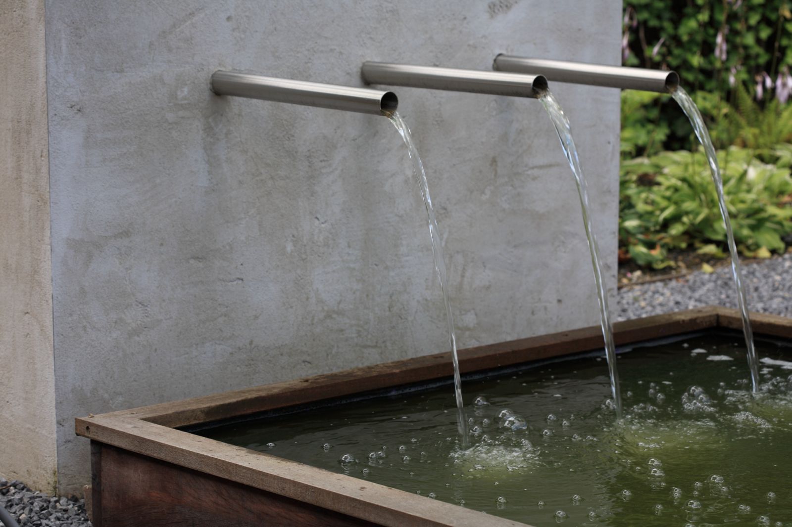 Moderne waterpartij met drie RVS spuiten op betonnen muur met waterstralen in houten bassin