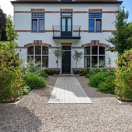 Witte villa met rode bakstenen accenten en voortuin met grindpad en groene beplanting