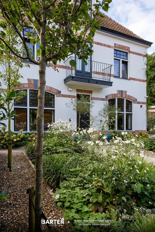 Witte villa met rode bakstenen accenten en voortuin met witte bloemen en grindpad