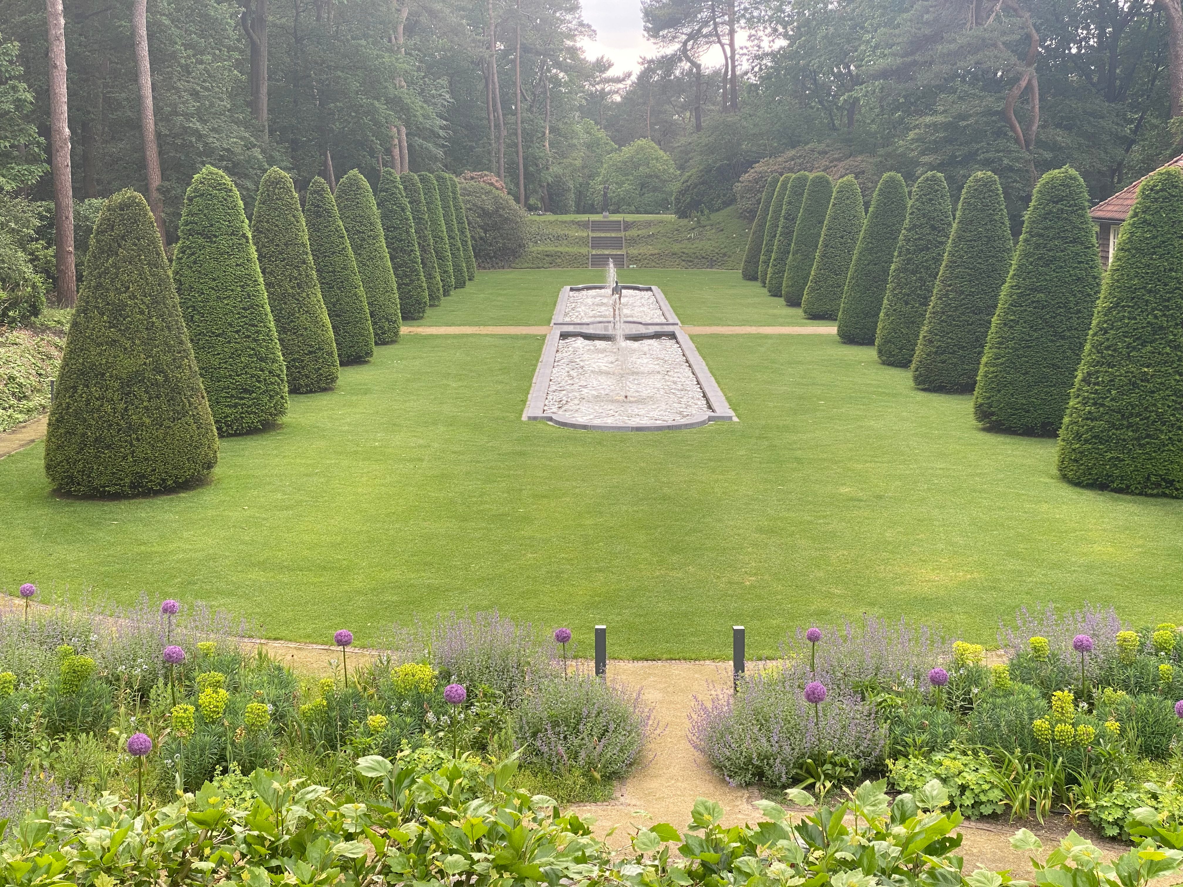 Formele as met waterpartij geflankeerd door grote kegelvormige taxusbomen