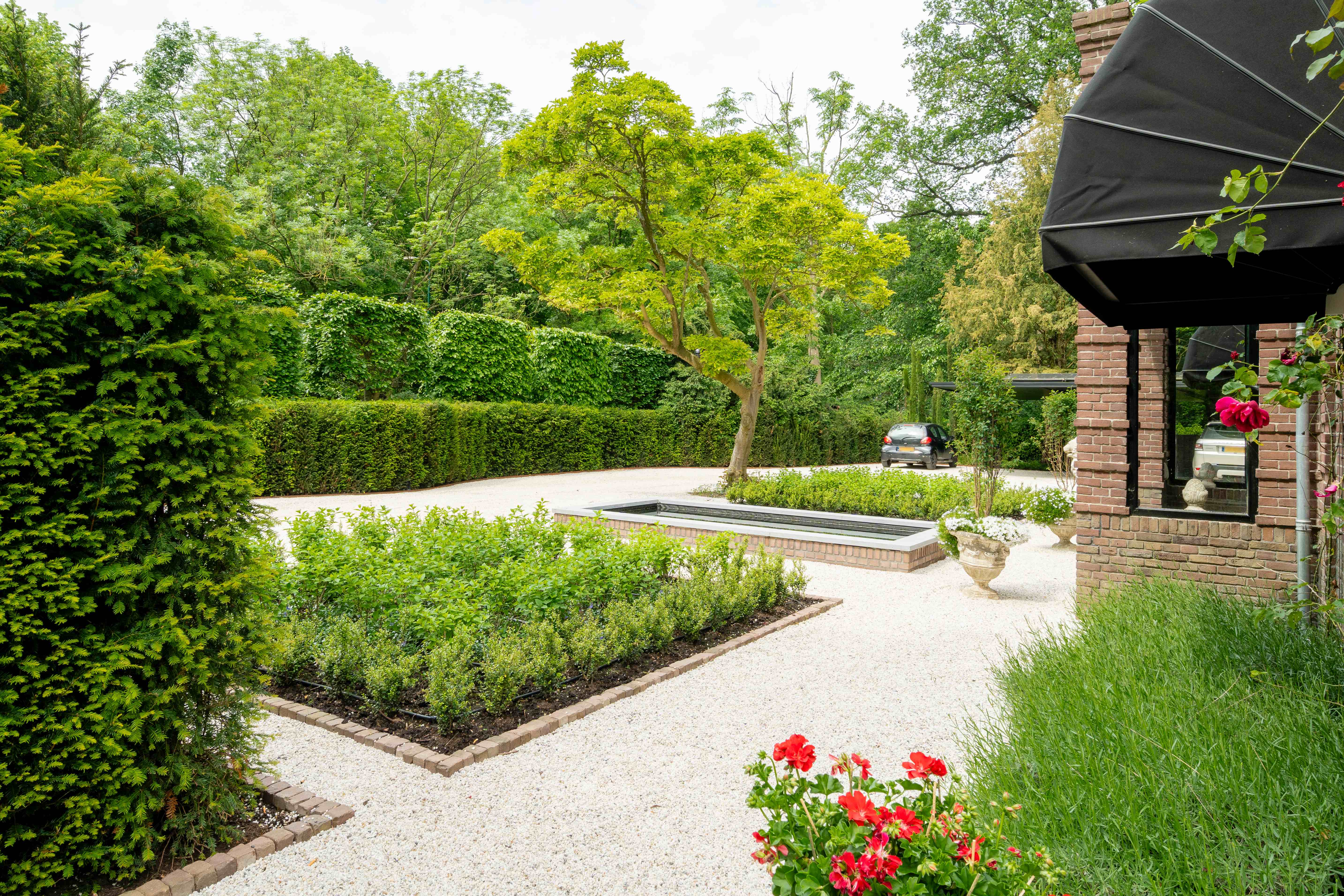 Voortuin met rechthoekige waterpartij, geschoren hagen en rode geraniums