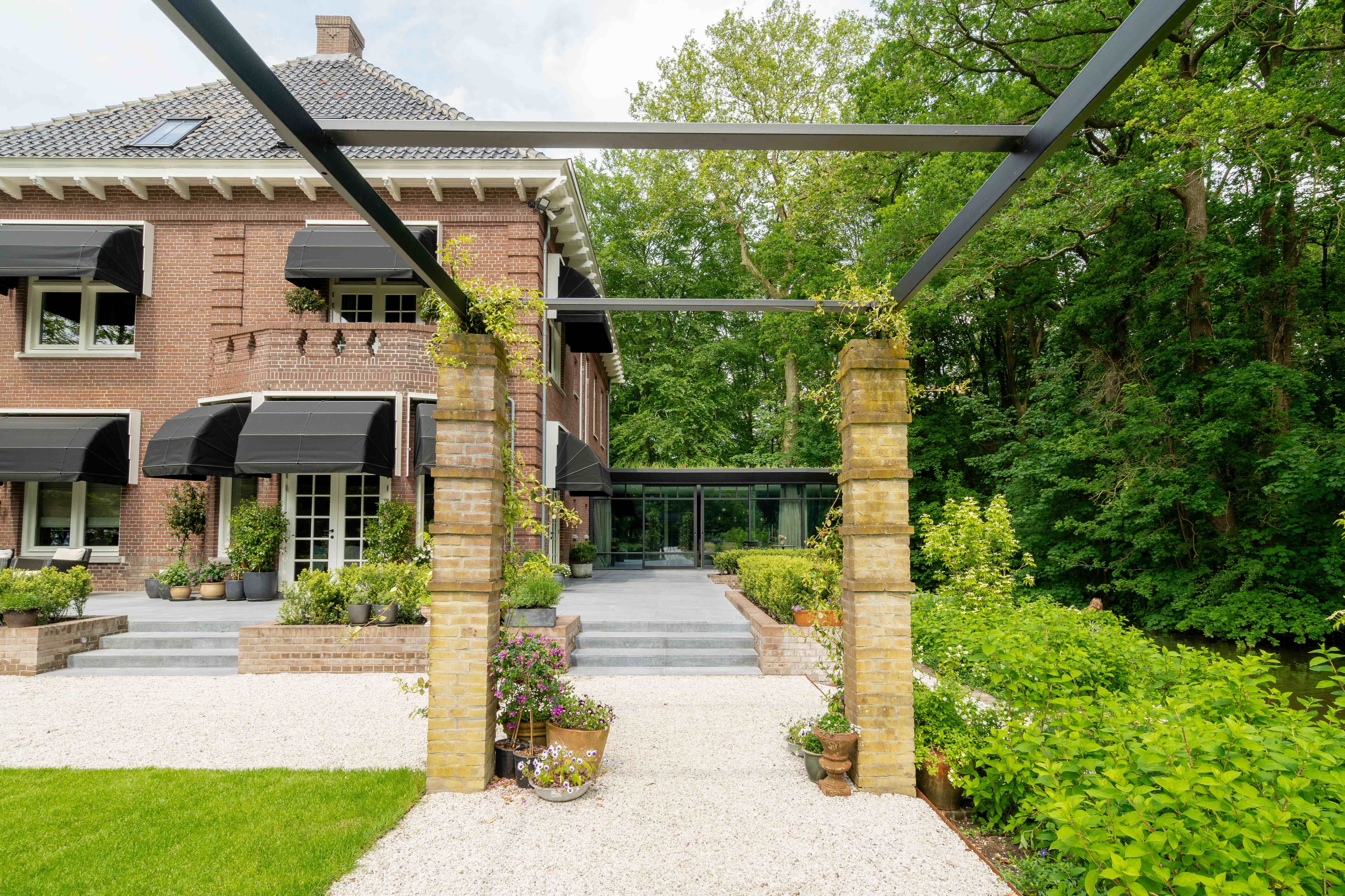 Elegante entree pergola met stenen zuilen en metalen raamwerk