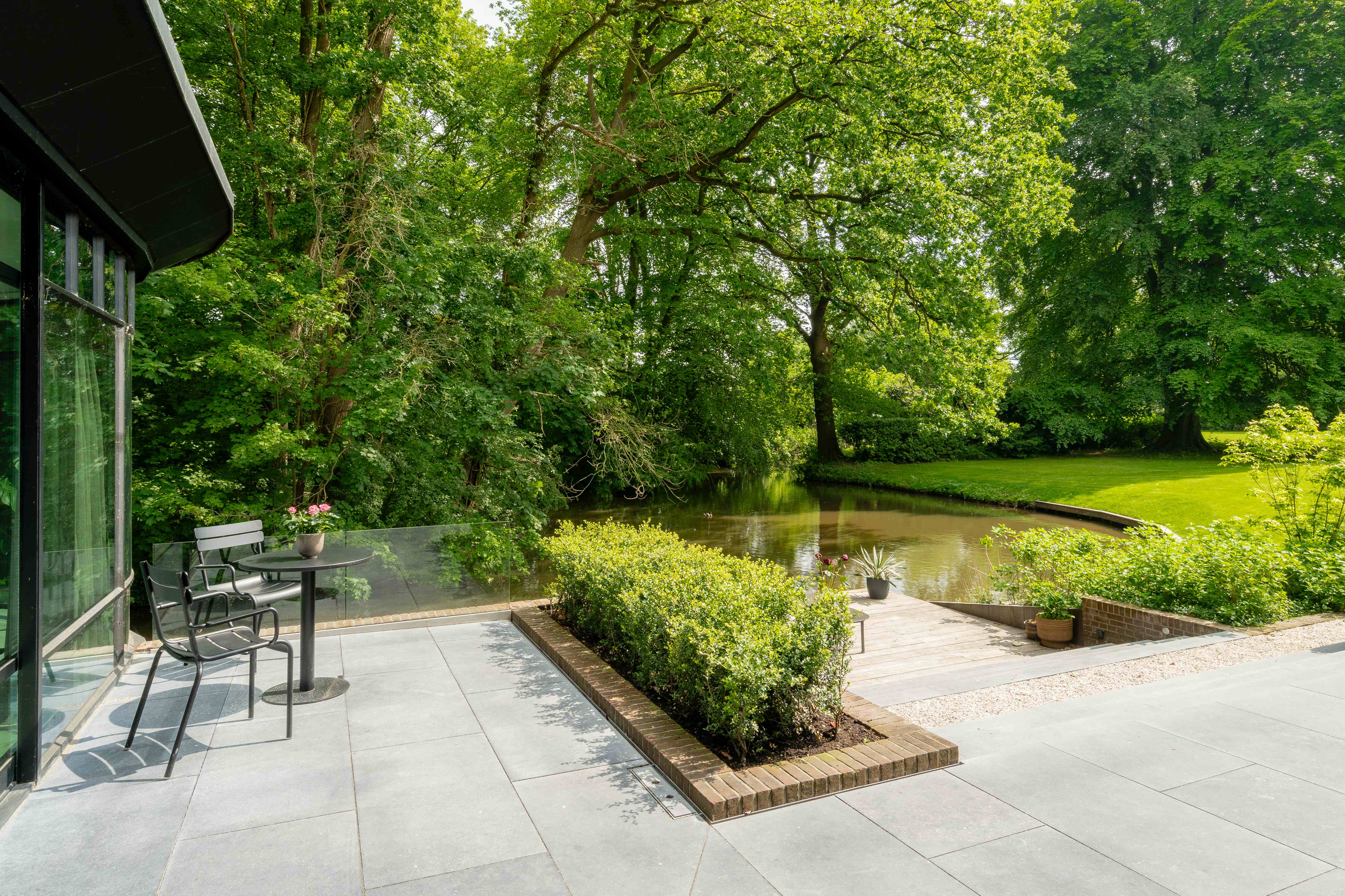Waterfront terras met geschoren buxus en uitzicht op natuurlijke vijver