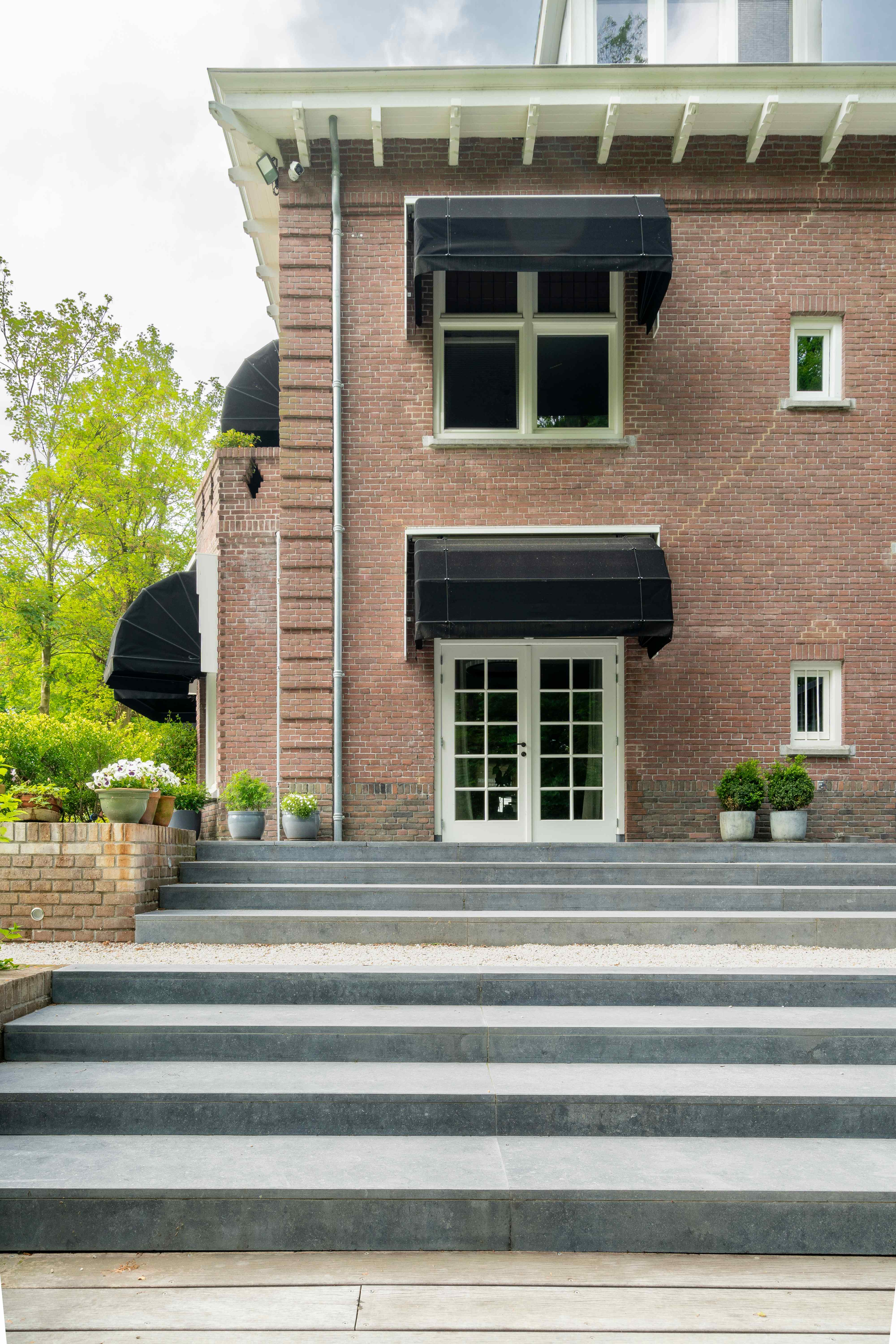 Elegante stenen traptreden naar bakstenen villa met zwarte luifels