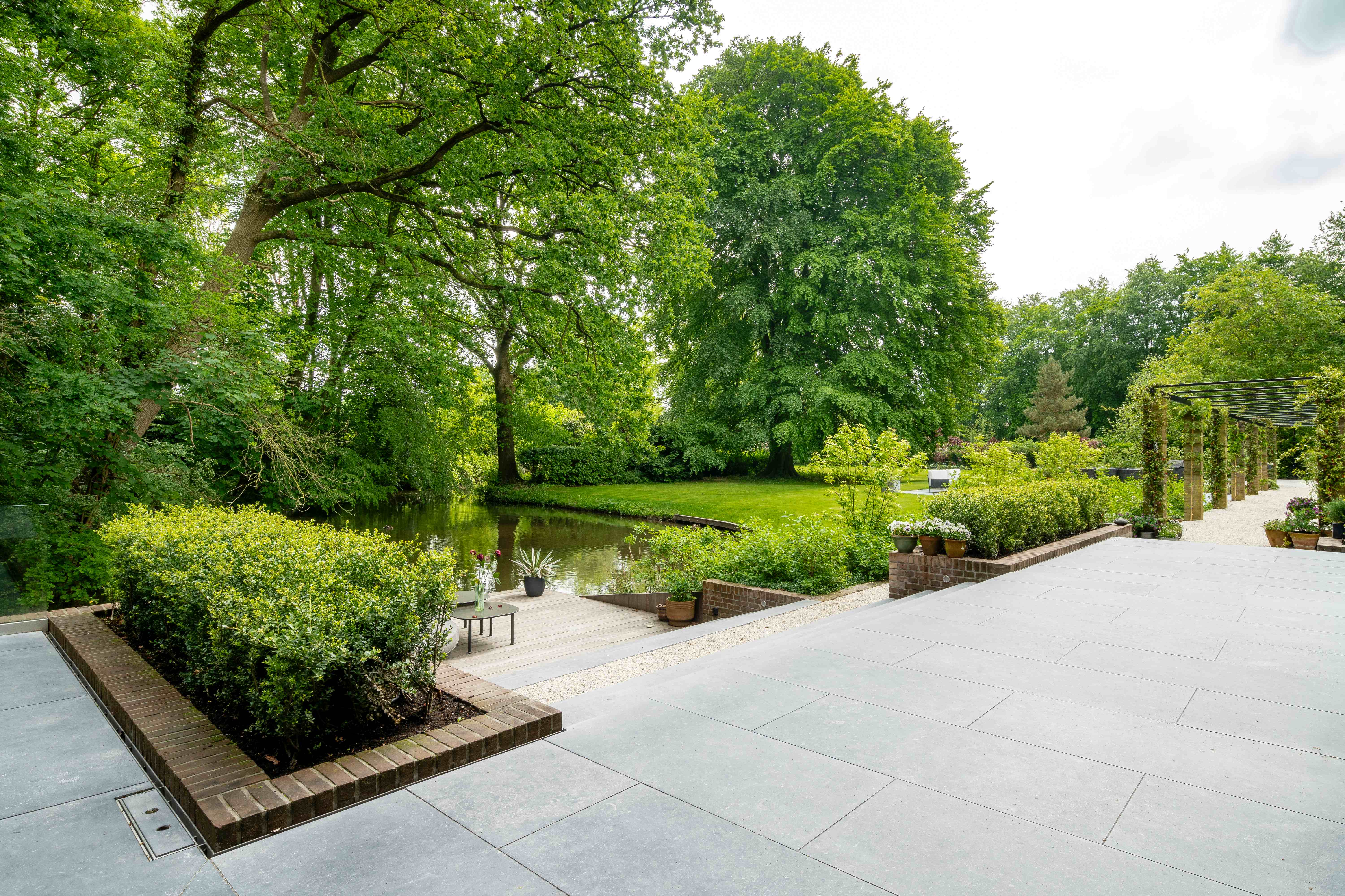 Tuinterras met waterpartij en pergola tussen weelderige beplanting