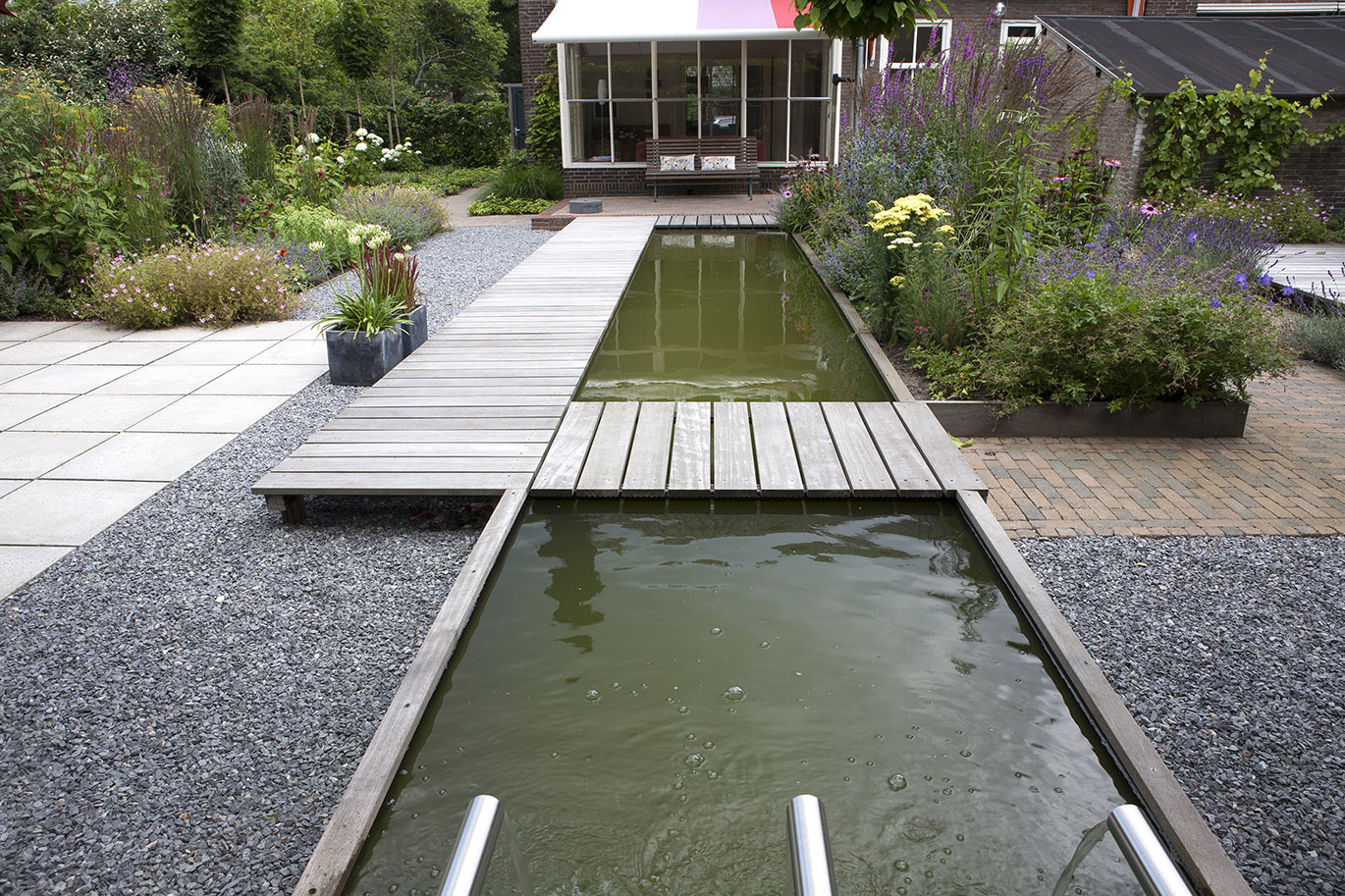 Zicht vanuit huis met houten vlonder over twee vijverdelen met waterpartij