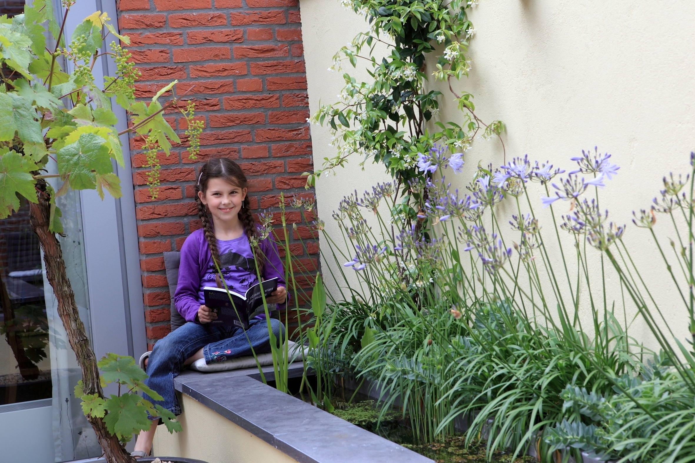 Kind zit lezend op rand van vijver met bloeiende Agapanthus