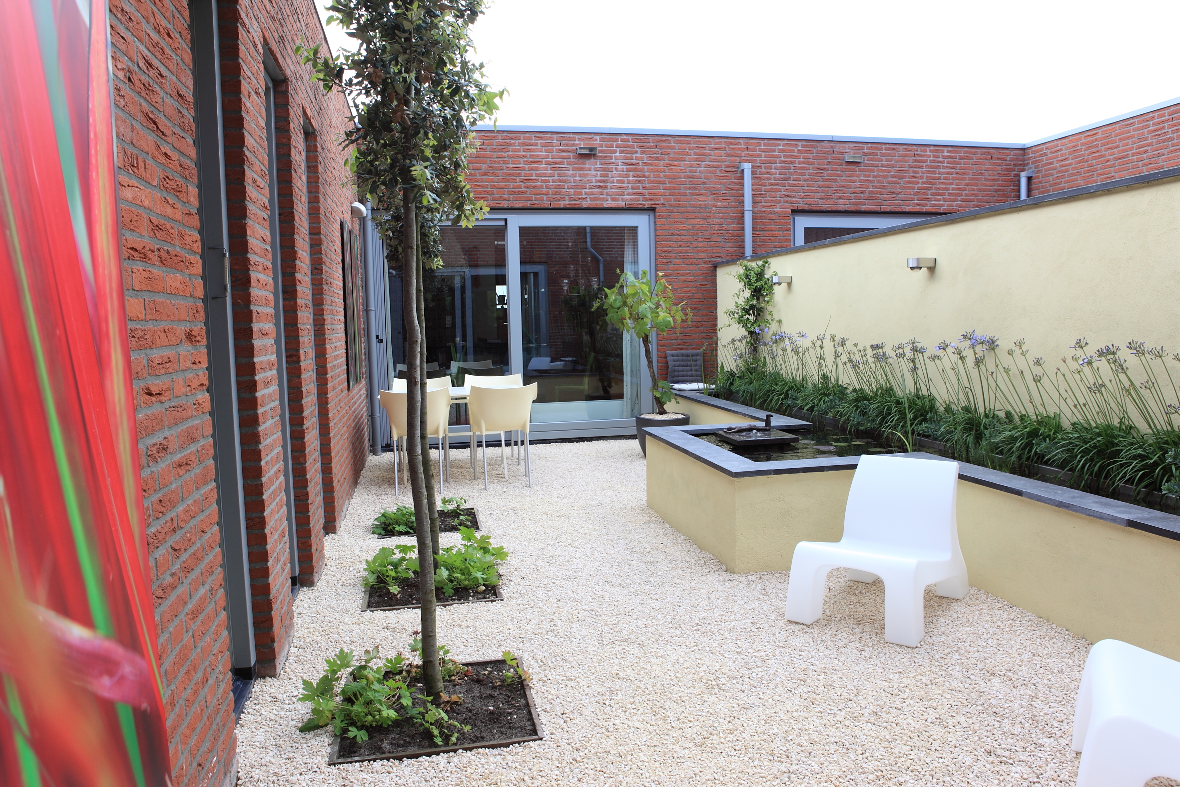 Overzicht patiotuin met verhoogde vijver, grindvloer en moderne stoelen