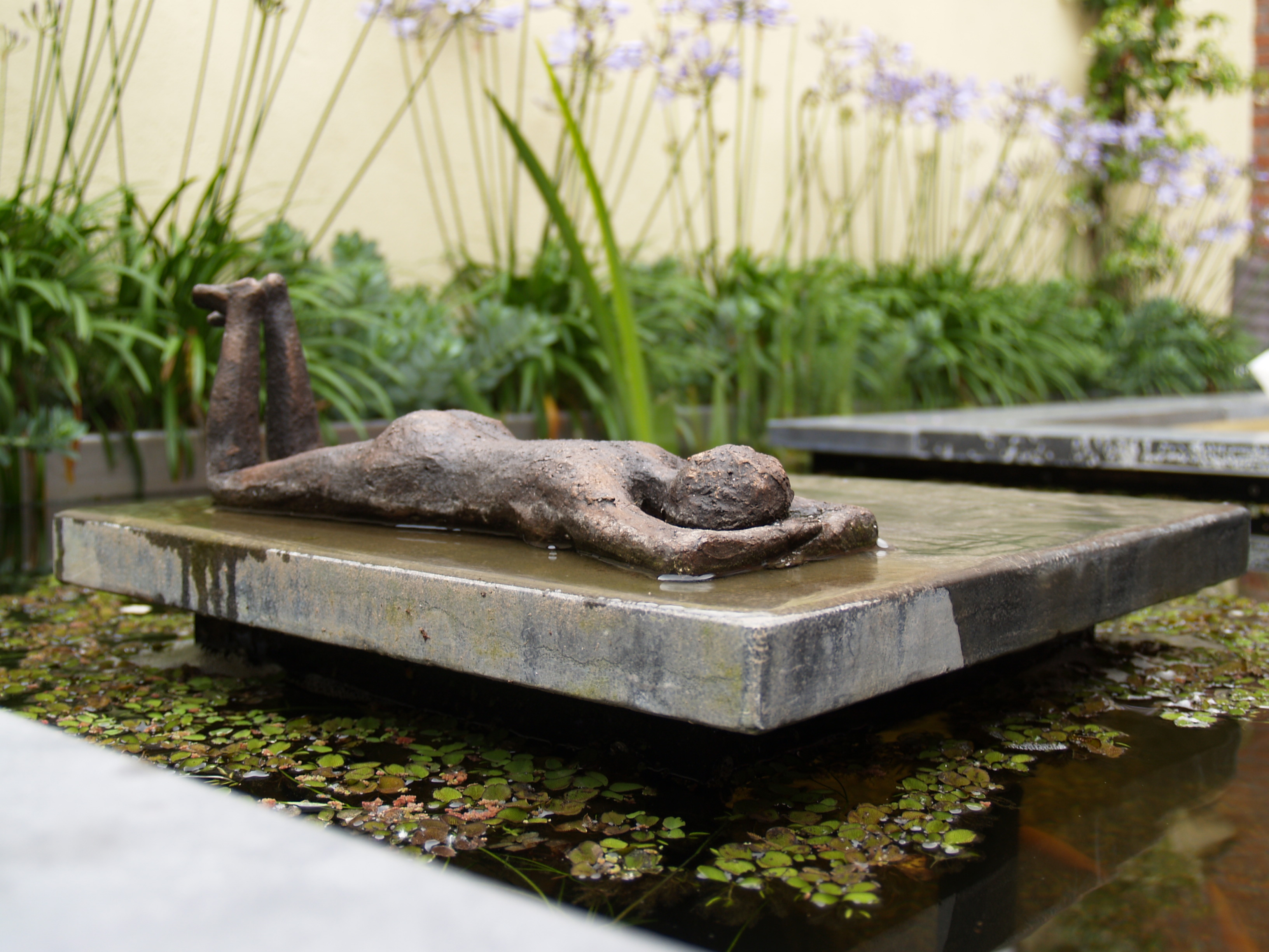 Bronzen sculptuur op stenen platform in vijver met waterlelies